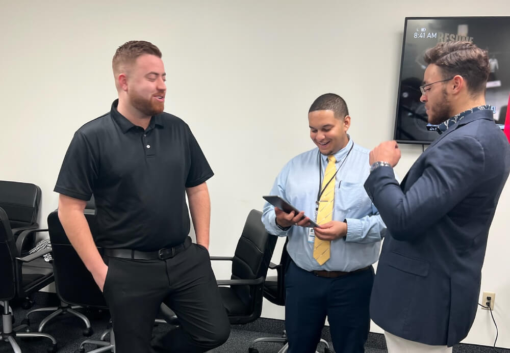 Three professional marketing consultants and reviewing digital performance data on a tablet in a clean office environment.