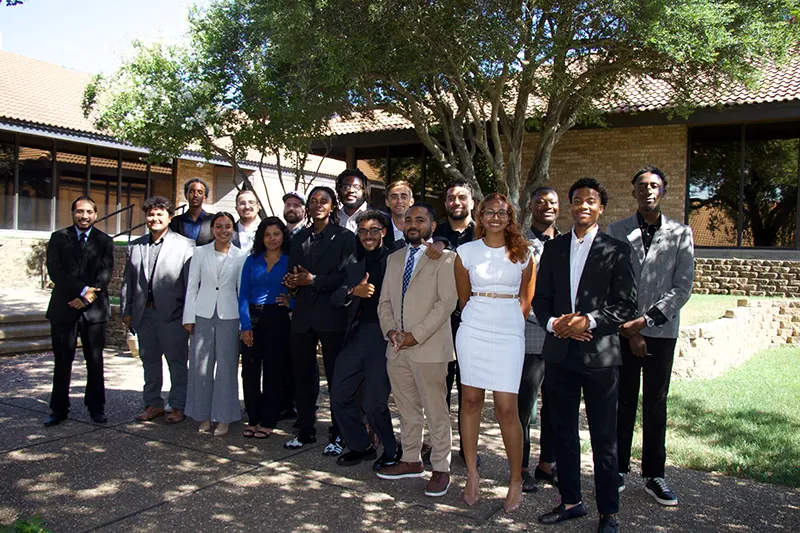 A diverse team of professional experts and direct marketing specialists standing together outside a modern corporate office building during a company retreat.
